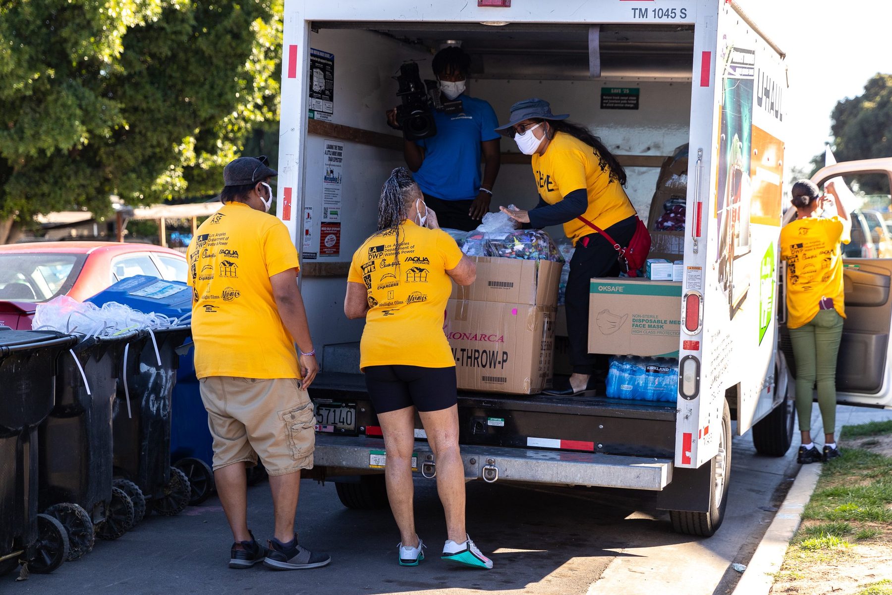 Warm the Streets volunteers in gold SERVE shirts unloading boxes of blankets and water from a truck in South Los Angeles
